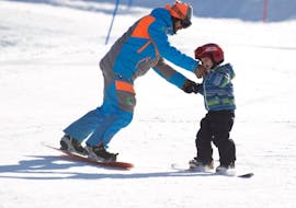 Istruttore di snowboard che aiuta un bambino a Limone durante una delle lezioni private di snowboard per bambini di tutti i livelli.