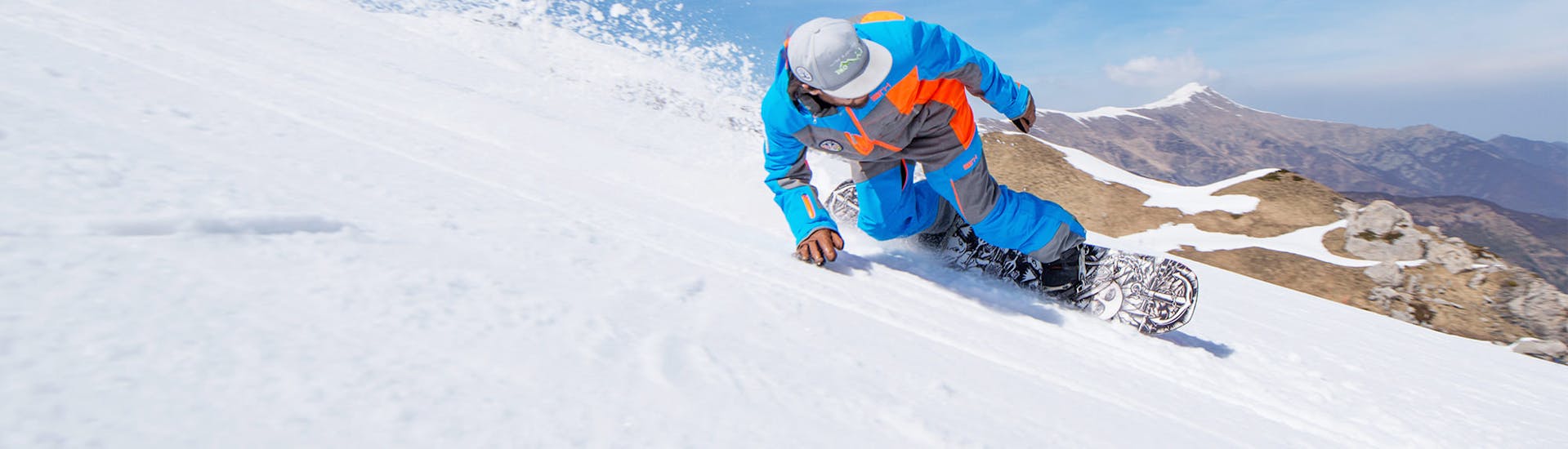Le moniteur de snowboard avec les magnifiques montagnes de Limone en arrière-plan avant l'un des cours particuliers de snowboard pour enfants et adultes de tous niveaux.