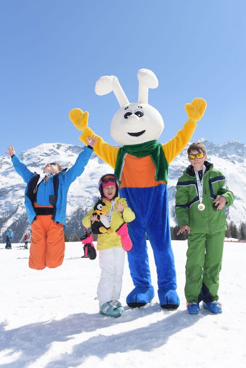 Les enfants s'amusent avec la mascotte Snowli lors du cours de ski pour enfants de l'École Suisse de Ski de St. Moritz the Red Legends.