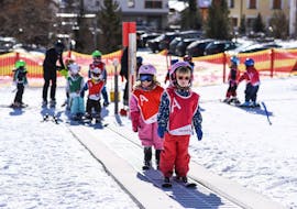 Two little skiers are taking the carpet lift during kids ski lessons in the Snowli Kinderland with Swiss Ski School St. Moritz.