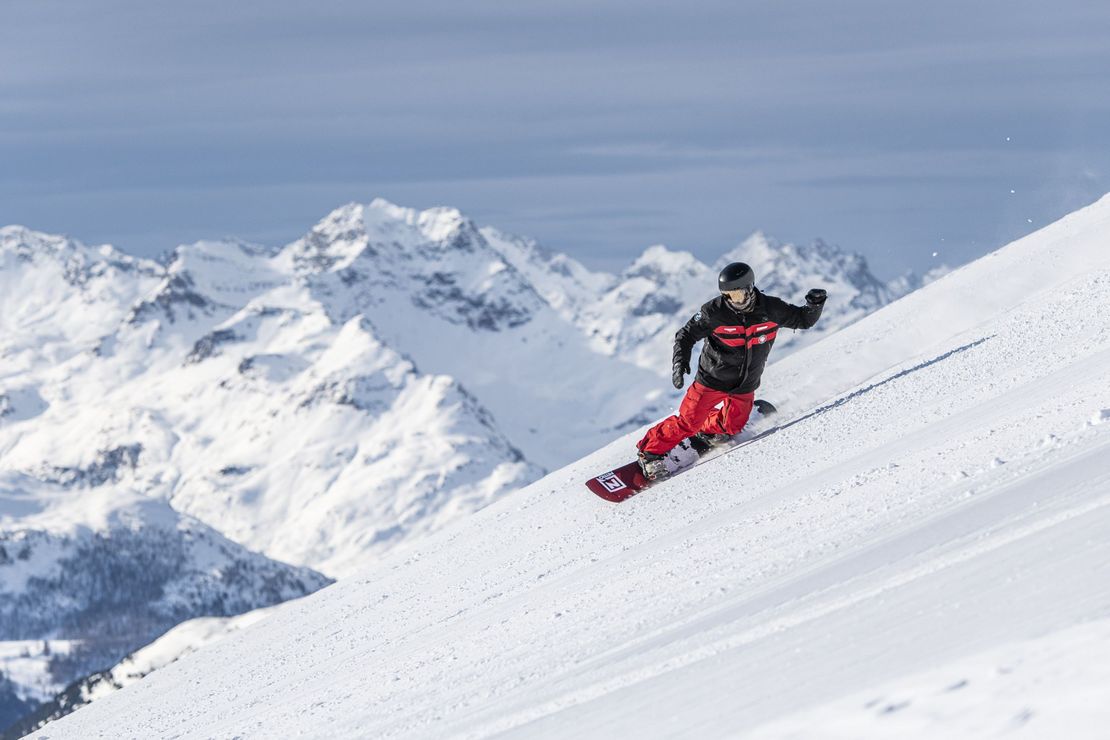 A snowboarder is going down the slopes of St. Moritz during private snowboarding for kids and adults of all levels with Swiss Ski School St. Moritz The Red Legends.