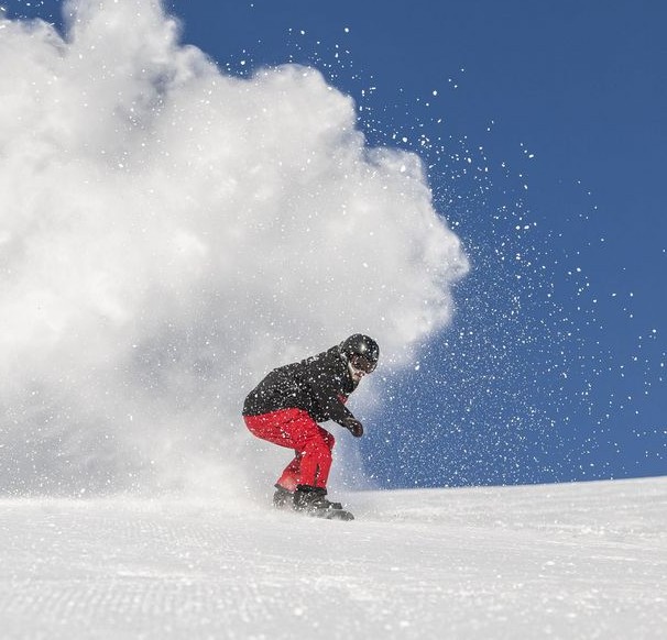 A snowboarder is going down the slopes of St. Moritz during private snowboarding for kids and adults of all levels with Swiss Ski School St. Moritz The Red Legends.