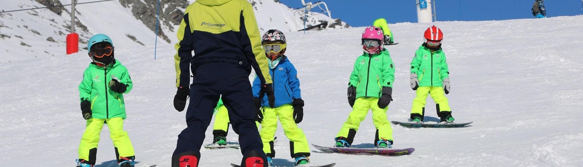 Un instructor de esquí de la escuela de esquí Prosneige Alpe d'Huez está enseñando a niños sonrientes, durante las clases de snowboard para niños de todas las edades y todos los niveles.