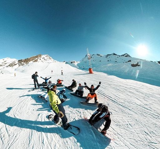 Snowboarders are sitting in the snow before their Adult Snowboarding Lessons for All Levels with Prosneige Alpe d'Huez.