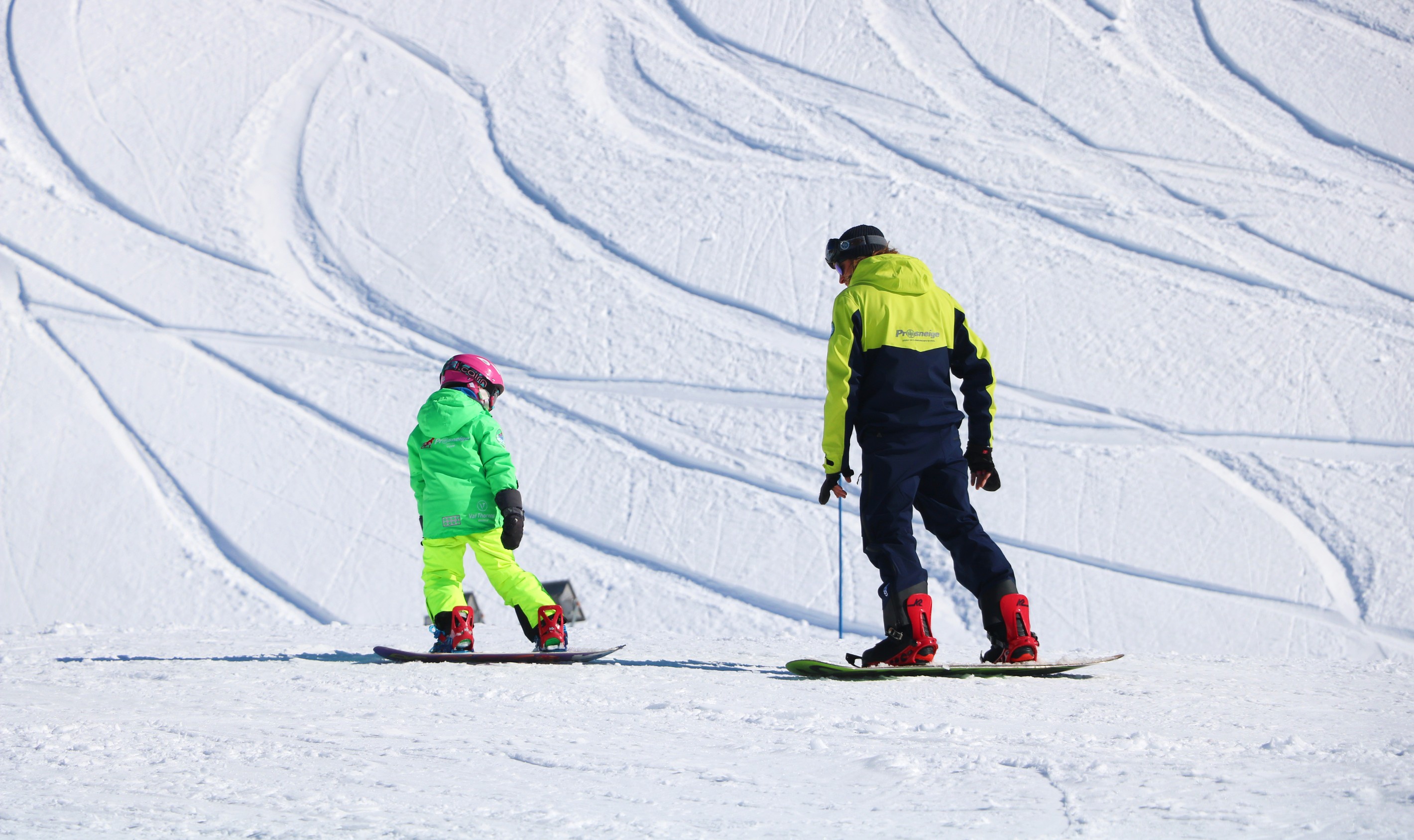 Un enfant apprend le snowboard sous l'œil attentif de son moniteur pendant un Cours particulier de snowboard avec Prosneige Alpe d'Huez.