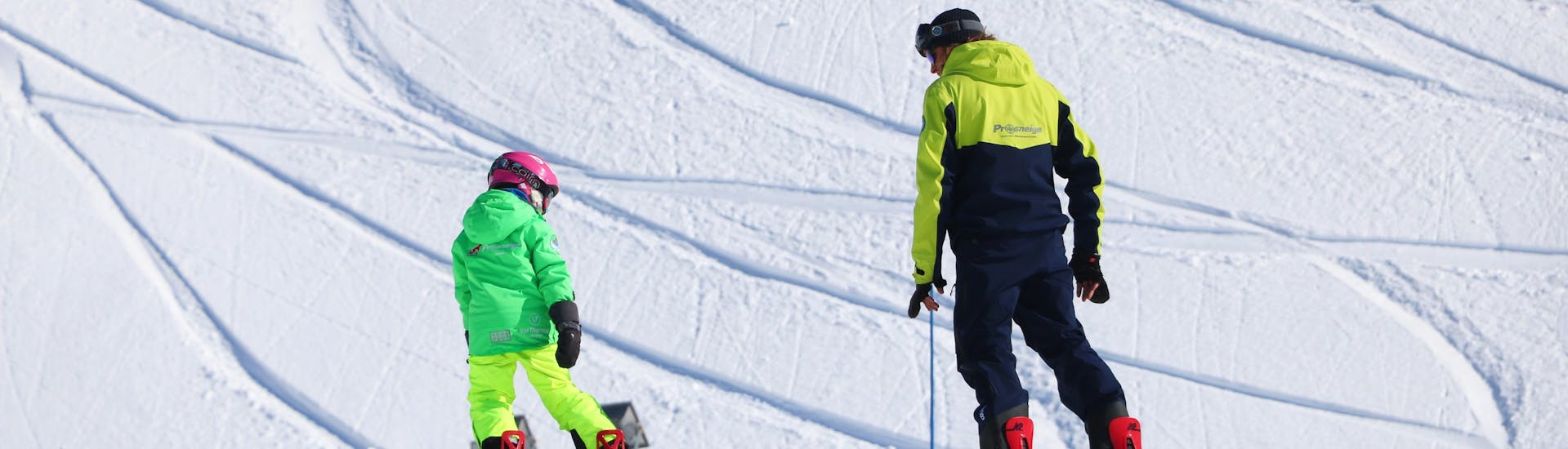 Un enfant apprend le snowboard sous l'œil attentif de son moniteur pendant un Cours particulier de snowboard avec Prosneige Alpe d'Huez.