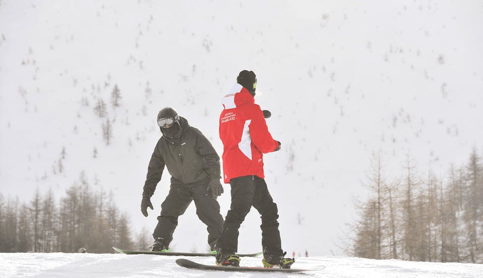 Ein Snowboardlehrer gibt einem Teilnehmer in Pragelato Tipps während einer privaten Snowboardstunde für Erwachsene für alle Levels.