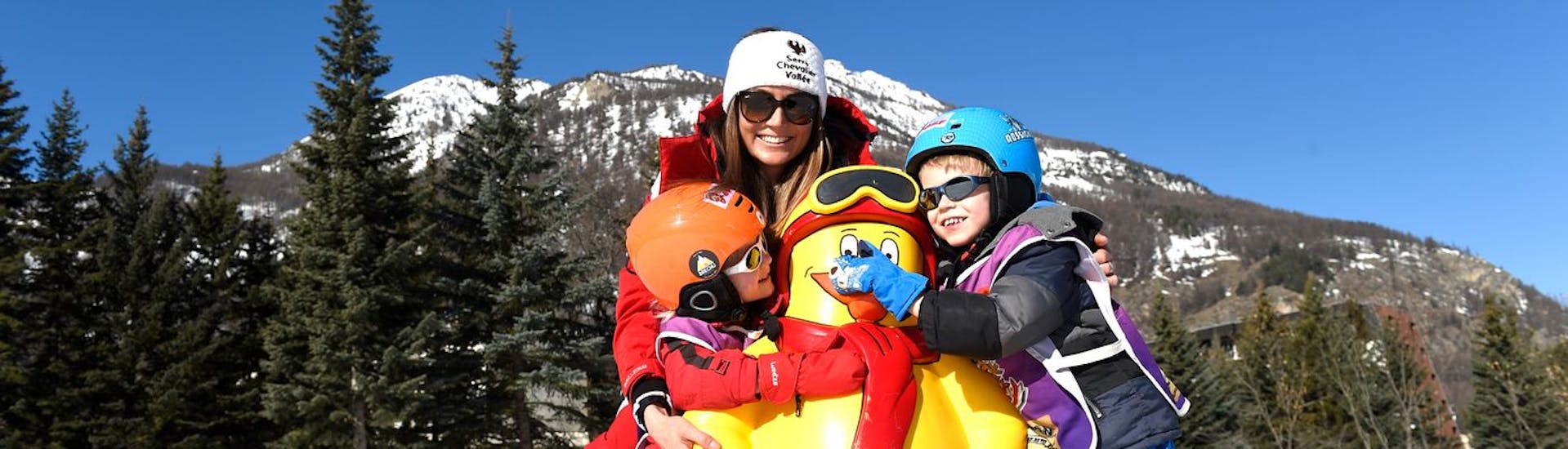 Kinder und ihr Skilehrer der ESF Serre Chevalier - Villeneuv haben Spaß mit Piou Piou während des "Baby Skieur" Kinderskikurses.
