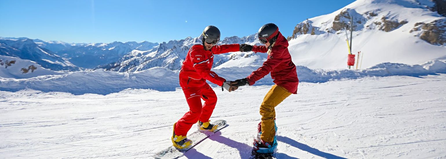 A snowboard instructor helps his student to keep his balance during a private snowboarding lesson for all levels with the Ski School ESF Serre Chevalier - Villeneuve.