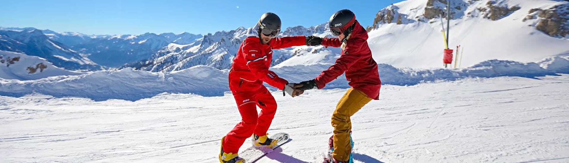 Un maestro di snowboard aiuta il suo allievo a mantenere l'equilibrio durante una lezione privata di snowboard per tutti i livelli con la Scuola di Sci ESF Serre Chevalier - Villeneuve.