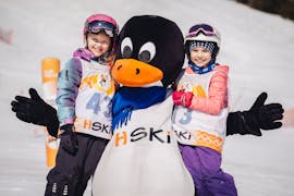 Zwei glückliche Kinder mit einem Pinguin-Maskottchen am Ende ihres Kinder-Skikurses für alle Stufen - Ganztag mit HSKI Zakopane.