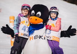 Two happy kids with a peguin mascot at the end of their Kids Ski Lessons for All Levels - Full Day with HSKI Zakopane.