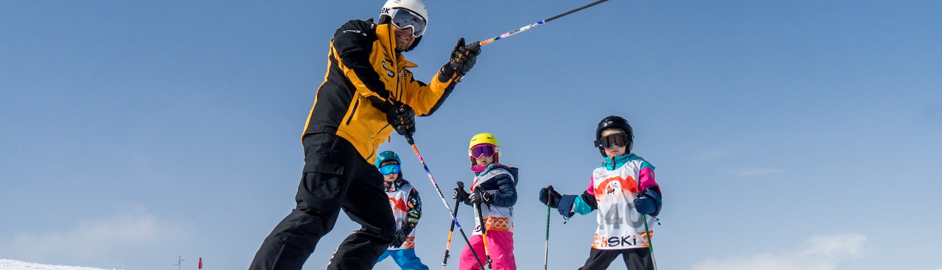 A ski instructor showing three kids the way on the slope during Private Skiing Lessons for Kids of All Levels with HSKi Zakopane.