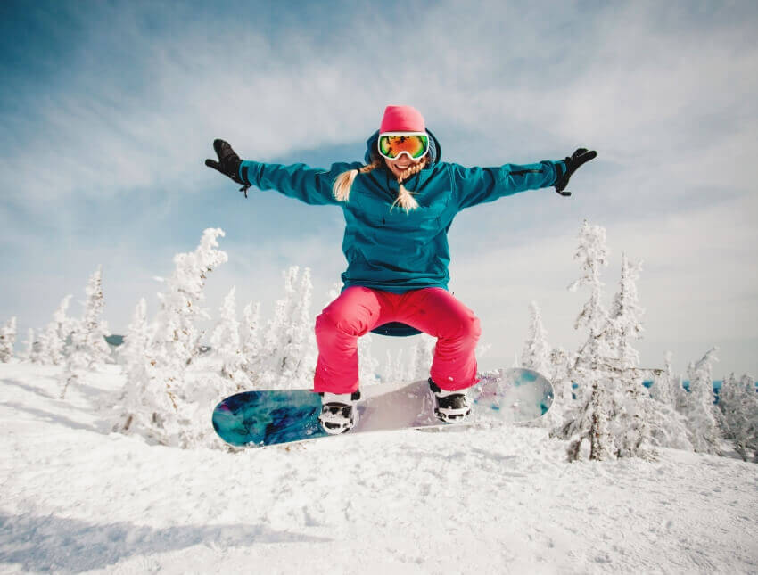 A snowboarder jumps in the snow in Saalbach-Hinterglemm during her snowboarding lessons for kids and adults for all levels with the OnSki ski school.