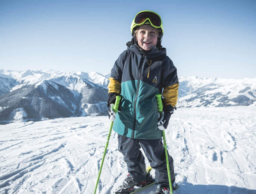 A little skier smiles at the camera during his private kids ski lessons with the OnSki ski school in Saalbach-Hinterglemm.