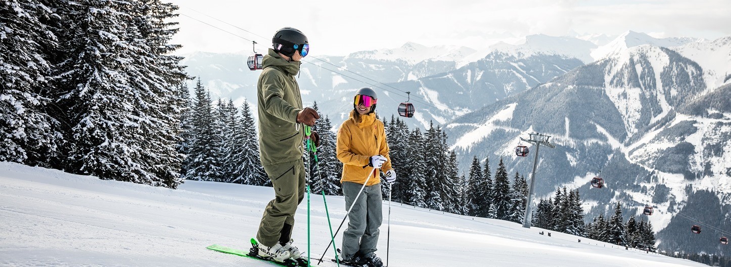Two skiers enjoy the view of the Saalbach-Hinterglemm ski area during their private ski lessons for families with the OnSki ski school.
