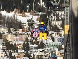 Una bambina sta prendendo la seggiovia durante le lezioni private di sci per bambini per principianti con Swiss Ski School Davos.