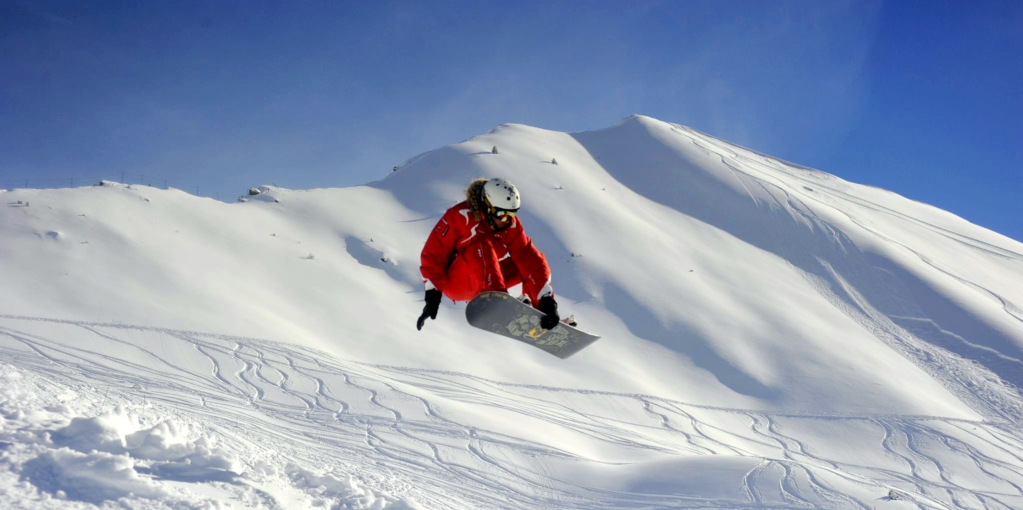 An instructor from the ski school ESF Ceillac does a snowboard trick during private snowboarding lessons for all levels. 
