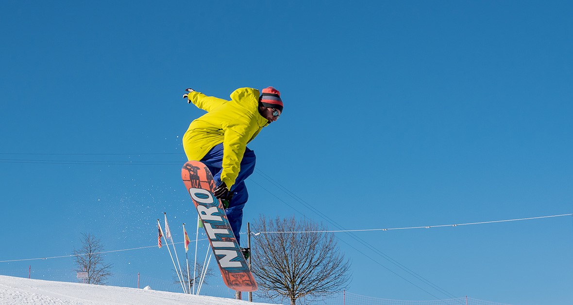 A ski instructor jumping in the air before one of the snowboarding lessons for kids and adults of all levels in Asiago.