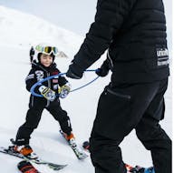 Beim Kinder-Skikurs (4-6 Jahre) für Anfänger wird ein Kind von einem Lehrer der Giorgio Rocca Ski Academy auf die Piste geführt.