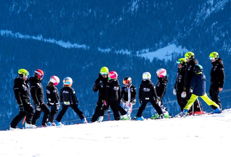 Gruppi di bambini si divertono sulle piste durante le lezioni private di sci per bambini con Giorgio Rocca Academy a Crans-Montana.