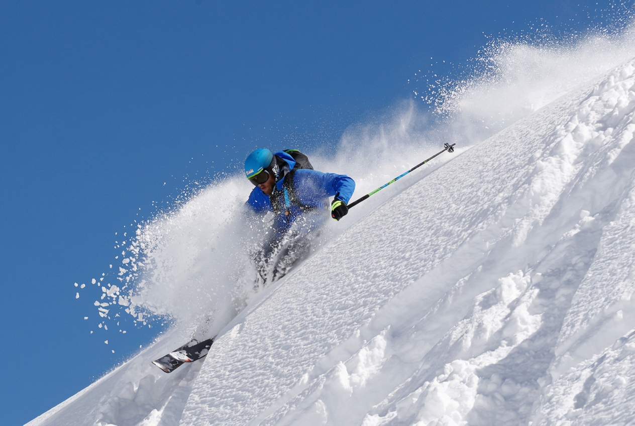 Un esquiador avanzado con chaqueta azul se abre paso entre la nieve polvo profunda en una pendiente pronunciada de la montaña durante una clase privada de esquí fuera de pista para esquiadores avanzados en la escuela de esquí y snowboard de Crans Montana.