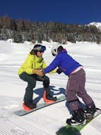 Un maestro di snowboard della scuola di sci Snowlimit Andermatt mostra gli esercizi a uno snowboarder durante una lezione di snowboard per bambini.