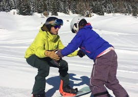 A snowboard instructor of the ski school Snowlimit Andermatt shows exercises to a snowboarder during a snowboarding lessons for kids.