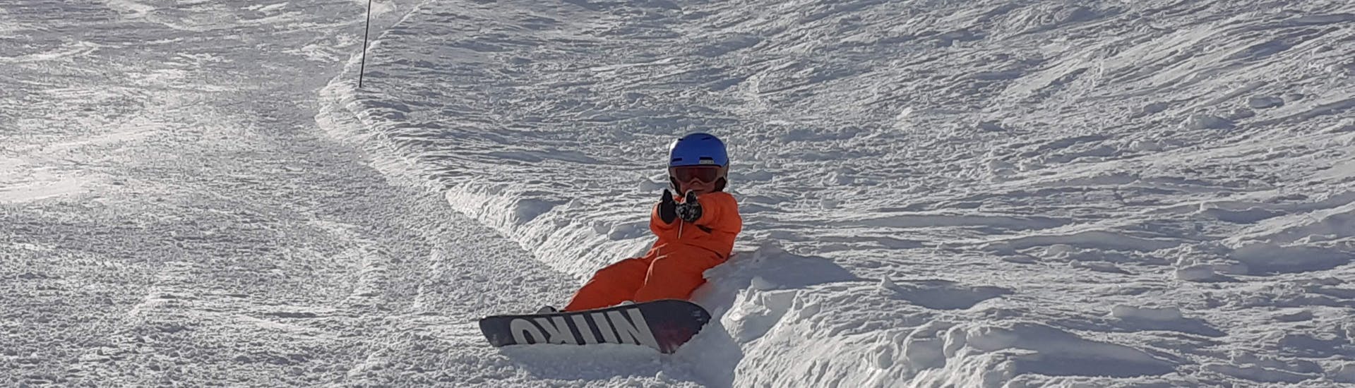 Een snowboarder zit naast de piste en geniet van de zon tijdens zijn privéles snowboarden (vanaf 5 jaar) voor alle niveaus.