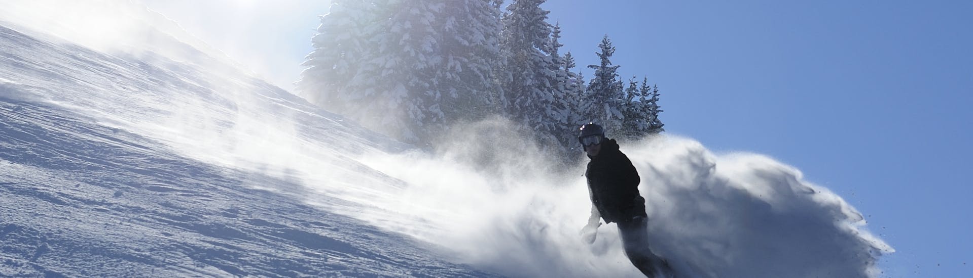 Ein Snowboarder rast während seinem privaten Snowboardkurs für Kinder und Erwachsene aller Levels mit der Schneesportschule Oberndorf die Pisten in Oberndorf hinunter.