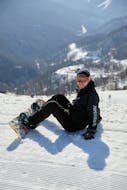 A snowboarder sits in the snow during his snowboarding lessons for kids and adults for beginners with the Nassfeld Ski School.