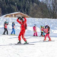 Een skileraar geeft les aan beginnende skiërs tijdens de skilessen voor beginnende skiërs "SkiLL Happy Kids" - 5 tot 14 jaar bij skiLL Saalbach Hinterglemm. 