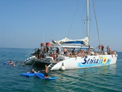 Persone che nuotano accanto alla barca di Catamaran Sensations Barcelona durante una gita in catamarano con barbecue intorno a Barcellona.