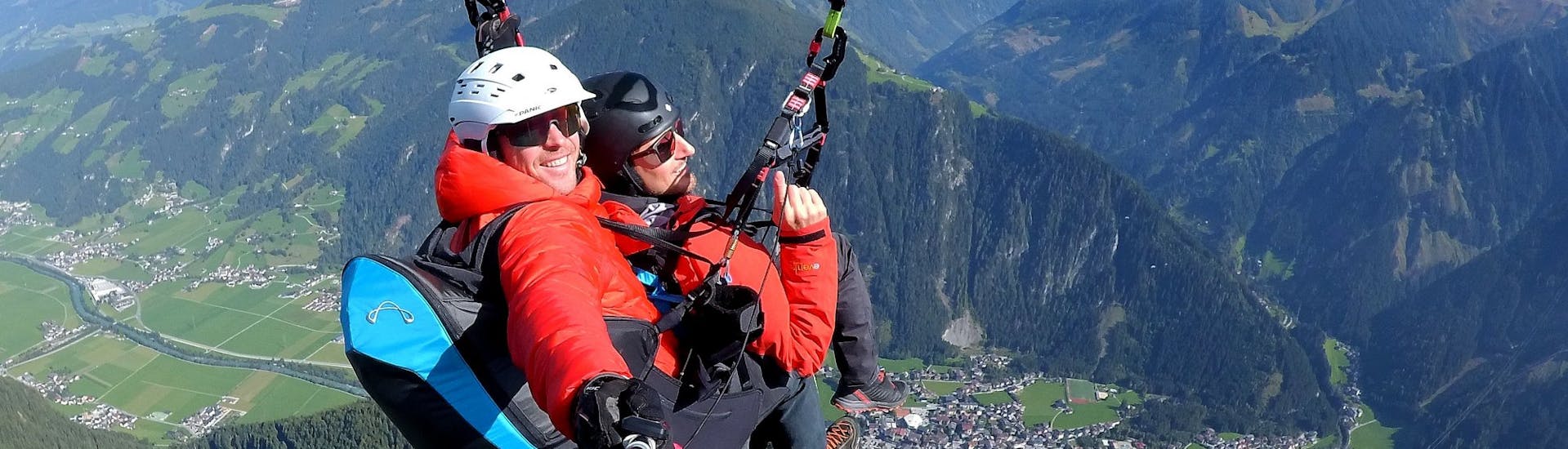 Een klant en zijn piloot van AIRflow Tandem Paragliding genieten tijdens hun Classic Plus vlucht in het Zillertal van het uitzicht op de bergen.