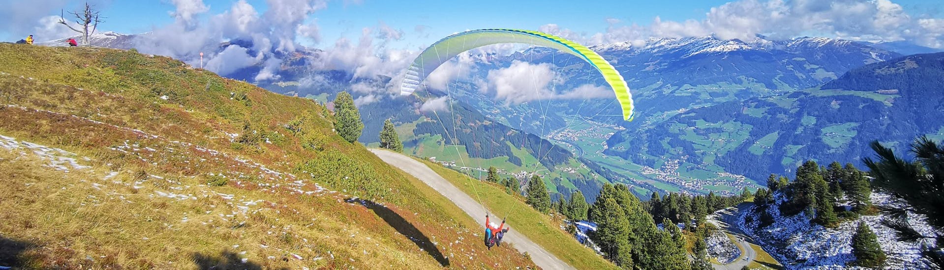 Der Pilot von AIRflow Tandem Paragliding Zillertal hebt mit dem Kunden für seinen gebuchten Tandem Paragliding Premium Flug in einer schönen Sommerlandschaft ab.