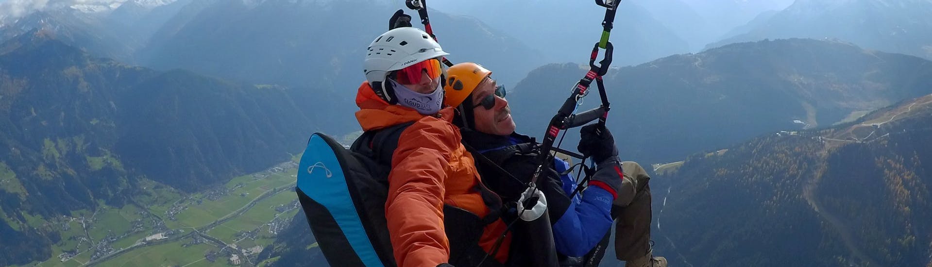 Een klant en zijn piloot kijken vrolijk in de camera terwijl ze door de lucht glijden tijdens hun tandem paragliding superior vlucht in het Zillertal door AIRflow Tandem Paragliding Zillertal.