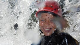 Een nat kind lacht in de camera tijdens Kids Canyoning in Loferbach mit Outdoor Guide Kaiserwinkl.