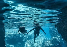 Vista subacquea di due nuotatori che entrano in una grotta durante il giro in barca di Capo milazzo con Milazzo Coast to Coast.