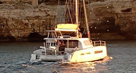 Vista di un catamarano di fronte alle scogliere di Polignano a Mare durante il Giro in catamarano privato alle grotte di Polignano a Mare con Pugliamare.