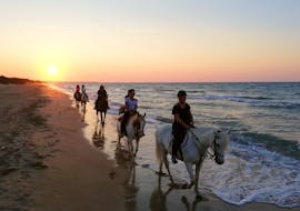 Un grupo de jinetes en la playa al atardecer durante el Paseo a caballo en el Parque Natural de las Dunas Costeras con Pugliamare.