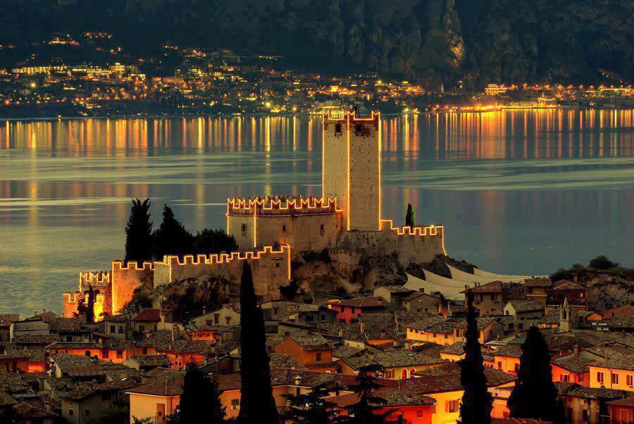View of the Malcesine Castle on Garda Lake at sunset with lights reflected on the lake during the Evening ride on Garda Lake to Malcesine - Round Trip with Garda Escursioni.