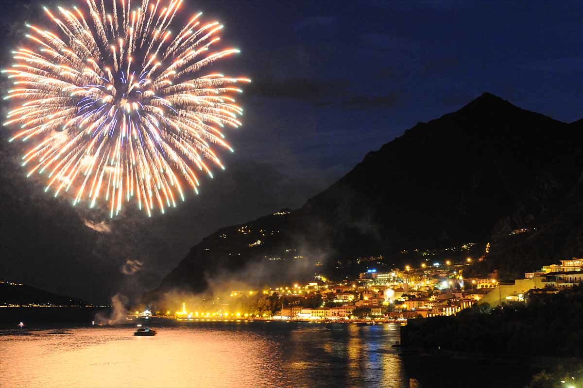 Uitzicht op het Gardameer bij nacht met vuurwerk en lichtjes die reflecteren op het wateroppervlak tijdens de Avondtocht op het Gardameer van Malcesine naar Limone met Garda Escursioni.