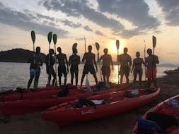 Vista di un gruppo di persone con pagaie e kayak con la luce dell'alba durante il Giro in kayak all'alba all'isola Proratora con snorkeling e caffè con Ecosport Sardinia.