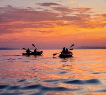 Four people on kayaks on the sea with the sunset light during the Guided Sunset Kayak Tour to Proratora Island with Snorkeling & Apéritif with Ecosport Sardinia.