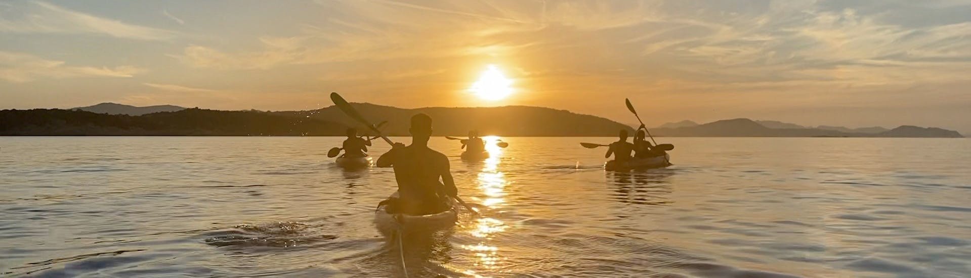 Un gruppo di persone pagaia sui kayak sul mare con la luce del tramonto durante il giro guidato in kayak al tramonto all'isola Proratora con snorkeling & aperitivo con Ecosport Sardinia.