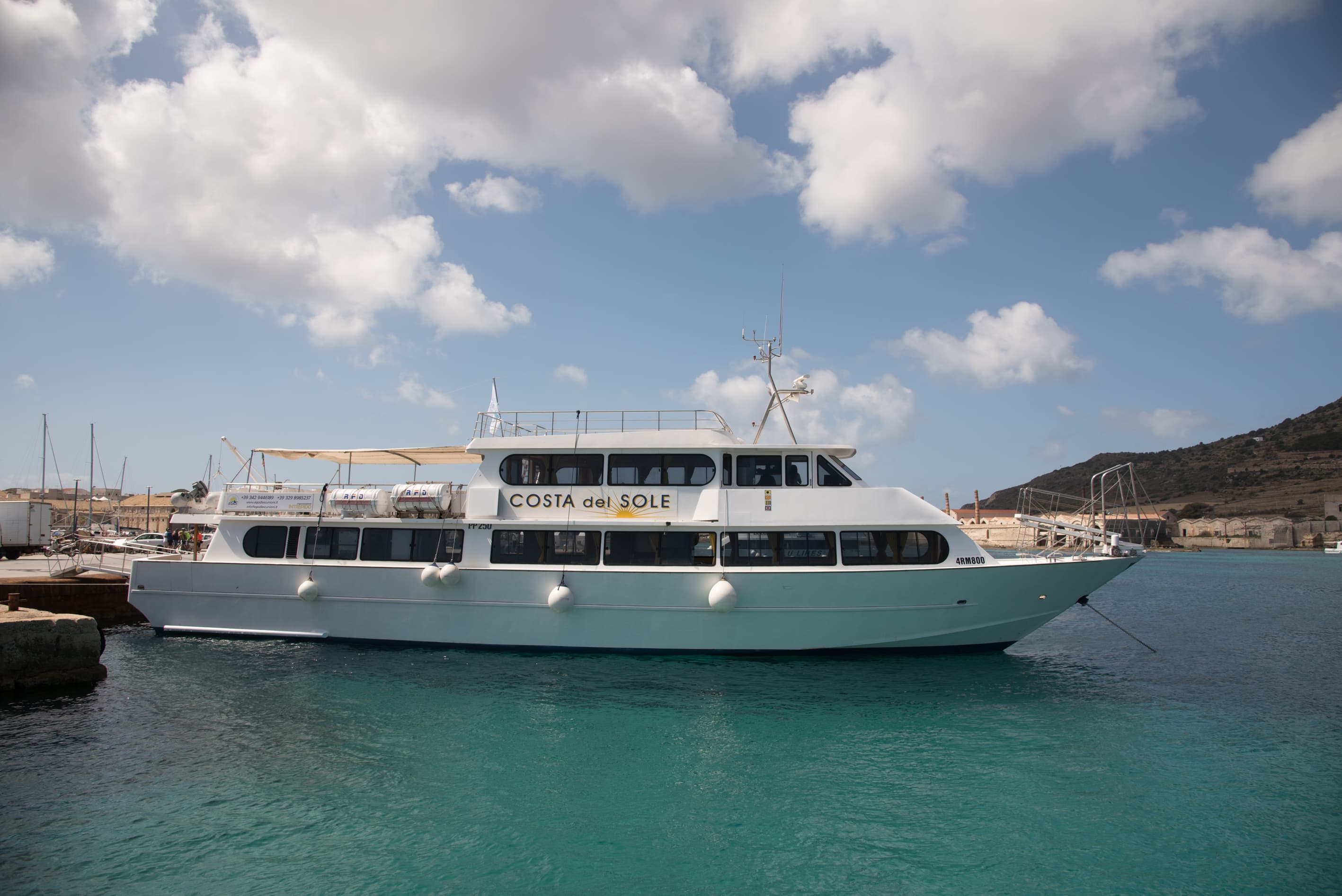 View of a boat moored at the port of Favignana with the panorama in the background during the Boat Trip to Favignana's creeks from Favignana with Egadi Escursioni.