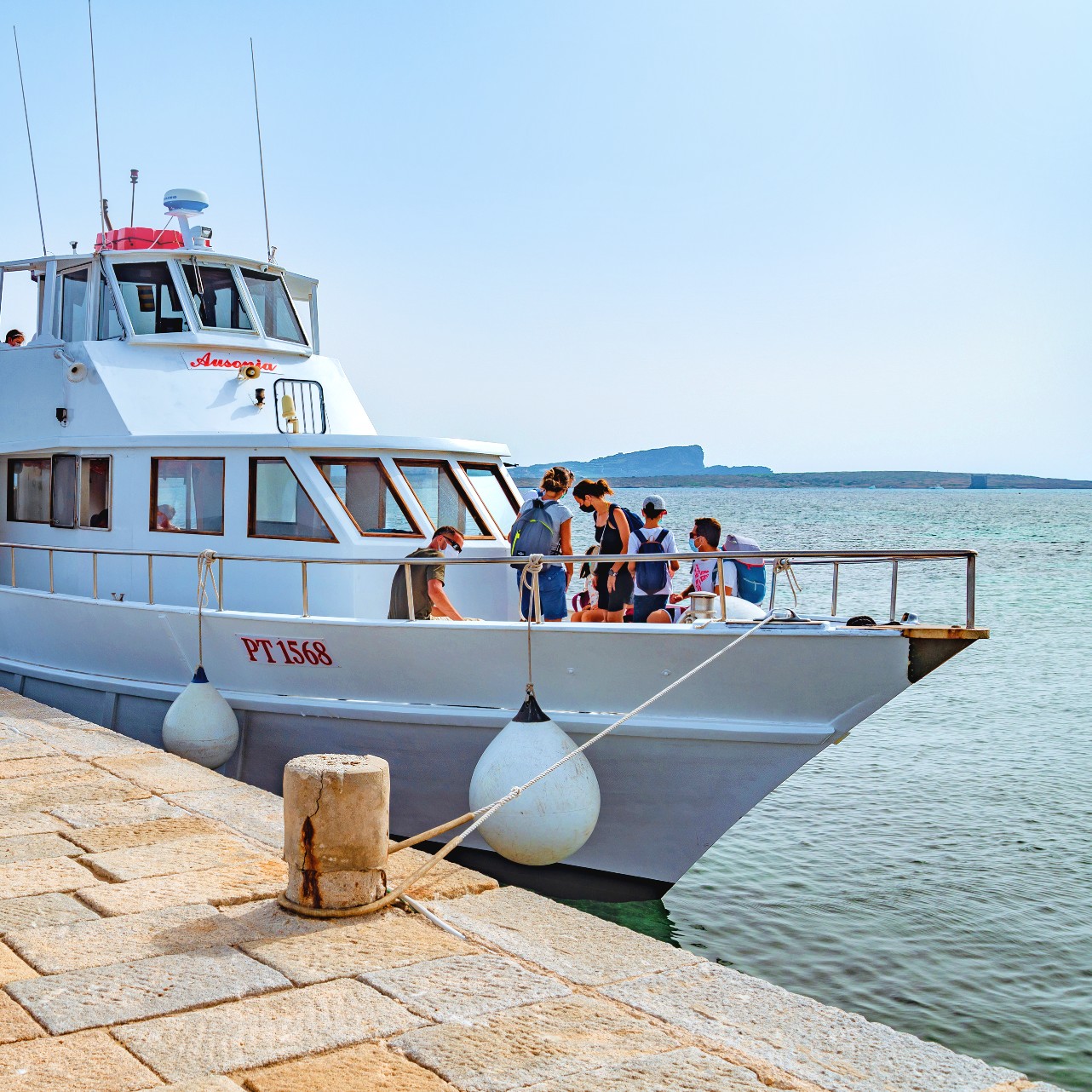 Personas a bordo de la motora Ausonia mientras está atracada en el muelle durante el traslado de Stintino a Asinara con la Linea del Parco Asinara.