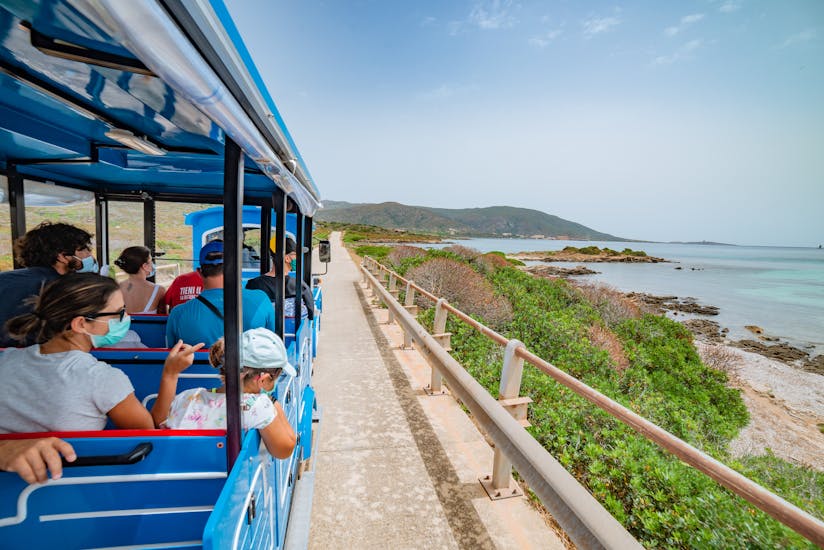 Menschen im kleinen Zug mit Blick auf die Asinara-Küste während der kleinen Zugfahrt mit Linea del Parco.