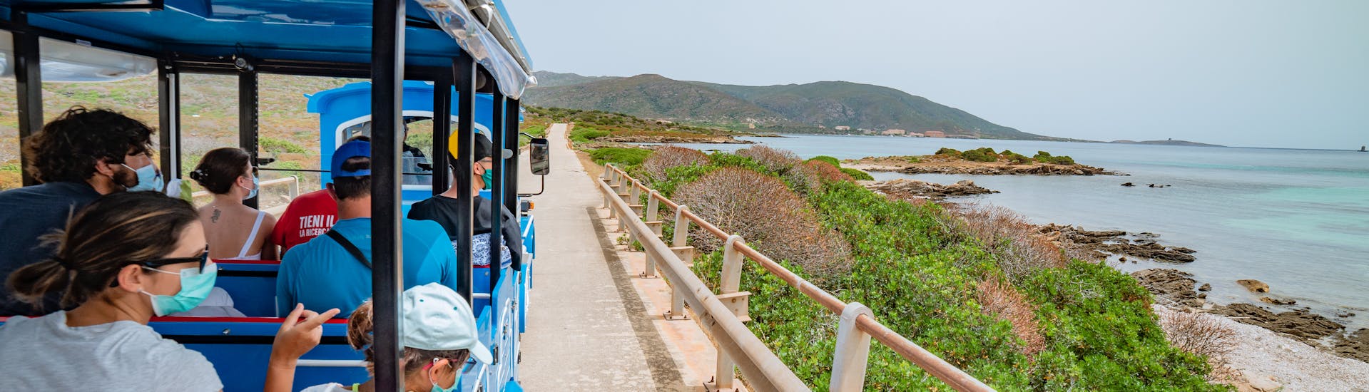 Persone sul trenino che guardano la costa dell'Asinara durante il giro in trenino con Linea del Parco.