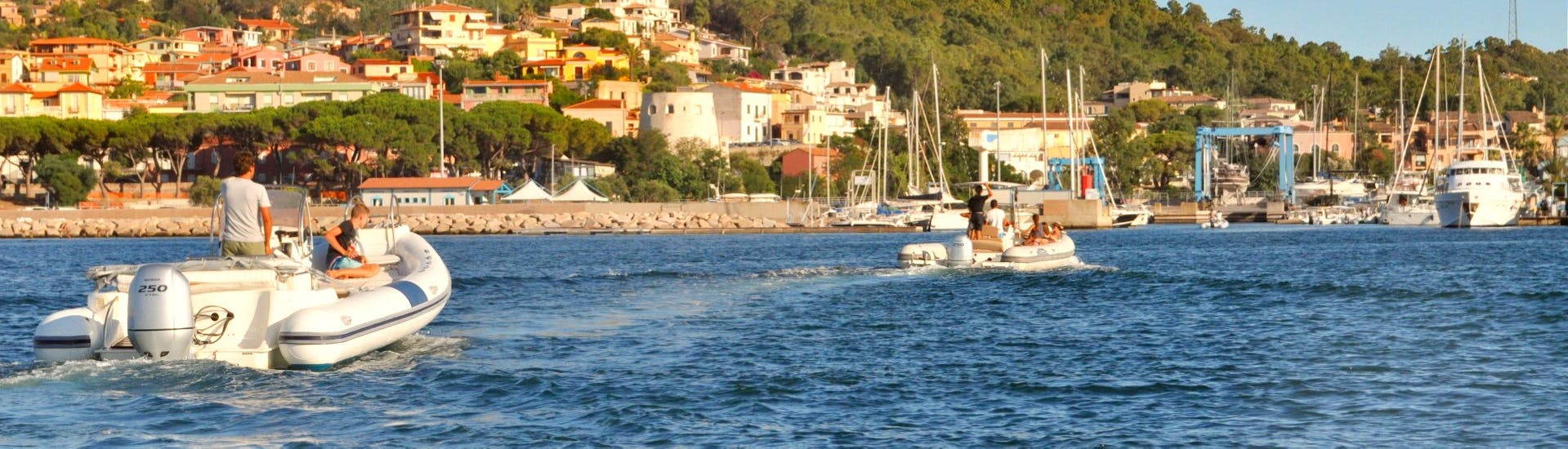 Due gommoni di Velamare Arbatax con persone a bordo che navigano uno dietro l'altro davanti alla costa.